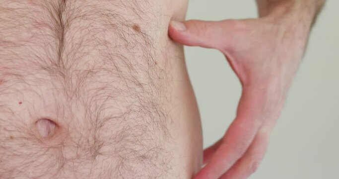 Caucasian male shirtless hairy abdomen grabbing and pinching his belly fat with left hand isolated shallow depth of field unrecognizable