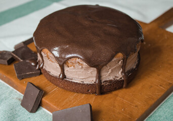 A fresh homemade cake is on a wooden board. Two sponge cakes and a cream layer in between covered with chocolate ganache and grated bitter chocolate. The process of making a cake at home