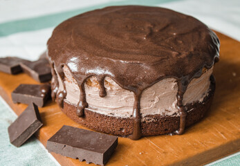 A fresh homemade cake is on a wooden board. Two sponge cakes and a cream layer in between covered with chocolate ganache and grated bitter chocolate. The process of making a cake at home