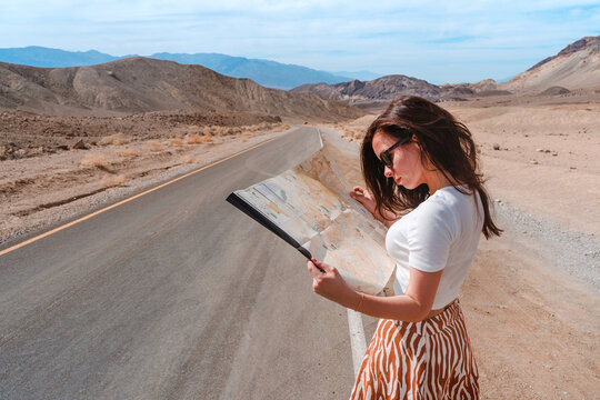 Beautiful young female tourist stands on an empty road with a map in Death Valley