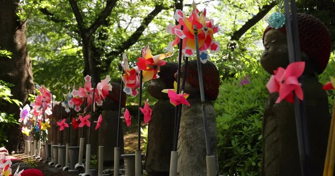 A slow motion of moving colorful windmills with Jizo statue daytime