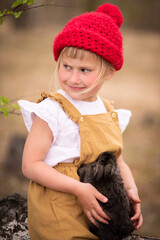 Little girl in a red hat in a spring forest plays with a rabbit in nature
