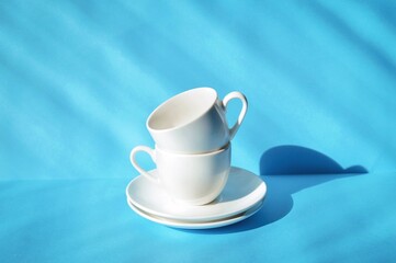 Fototapeta na wymiar Cup and saucer on a blue table. White porcelain tableware set, clean dishes. Kitchen poster 