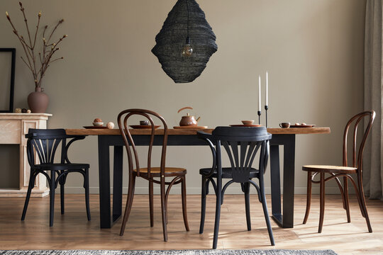 Stylish rustic interior of dining room with walnut wooden table, retro chairs, decoration, fireplace, dried flower, candlestick mock up picture frame and carpet in minimalist home decor. Template.