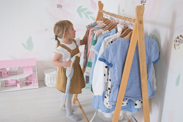 A little girl chooses clothes and puts things in order in the room, a child tries on dresses in a bright children's room