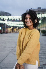 Happy african american woman with yellow outfit and headphones listening to music in the street at night