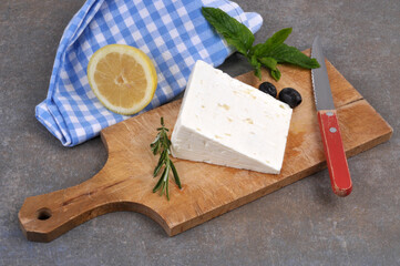 Morceau de feta sur une planche à découper avec un couteau, des olives noires, du citron et du romarin en gros plan