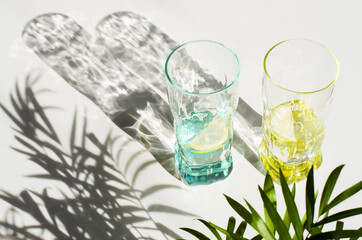 Lemon drink, fresh lemon and glasses. Summer tropical composition, vacation refreshment concept. Long harsh shadows. Summer and holiday mood. Flatly, top view, yellow
