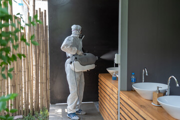Professional technical man in prevention suit with his sterilizing machine and disinfecting water sprays in toilet or wc area field for purifying coronavirus (COVID-19).