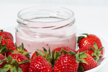 strawberry yogurt in glass jar and fresh berries on white background, closeup