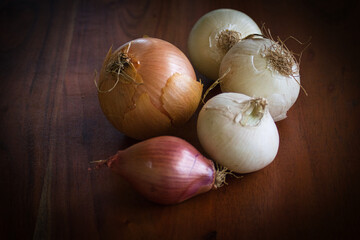 Verschiedene Zwiebelarten in Nahaufnahme auf einem dunklen Holztisch