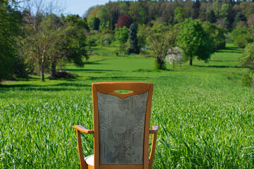 Ein Stuhl in Rückansicht vor einer grünen Wiese mit Streuobstbäumen und einem Wald im Hintergrund