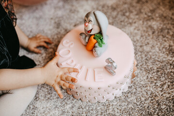 Child reaching a cake with marzipan decorations and a candle.