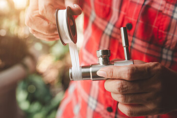 Asian Man Plumber in Plaid shirt winds seal tape on a thread of a plumbing fitting, two hands wrapped water tap or faucet for Connect the pipe, Close-up