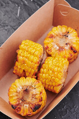 grilled corn in a craft container on an isolated dark background. Photo for menu and site. space for text. Close up