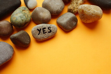 Pebble stone with the text yes on an orange table in a heap of pebbles