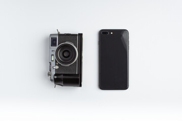 A mirrorless camera and smartphone lays aside on a white background