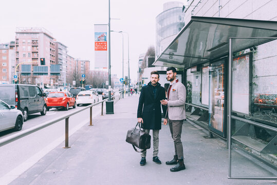Two young successful bearded business men outdoor using smartphone bus stop