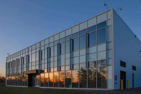 Low-rise commercial or institutional building glass and aluminum facade at dusk with sunset reflecting on windows, security cameras, nobody