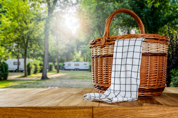 Wooden table with wicker basket for camping on a sunny holiday day. 