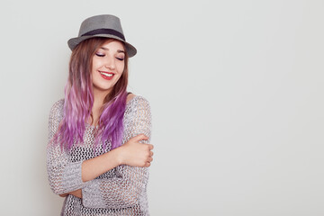 Pleasant looking dreamy female with purple hair hugging herself and keeping eyes closed, expressing happiness, copy space for advertisement, isolated over white background.