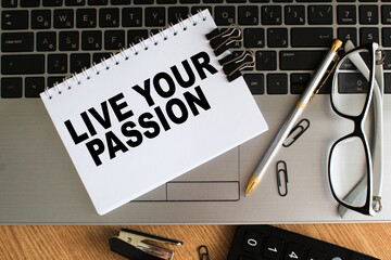 A notebook with text LIVE YOUR PASSION on the office desk, a laptop with stationery. A blank notepad for entering a copy or text. business