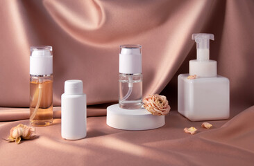 Cosmetic products and dry rose on pink shiny textile background. White and clear bottles of face and body products. Beauty concept