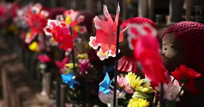 A slow motion of moving colorful windmills with Jizo statue daytime closeup