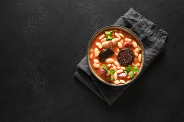 Spanish fabada with chorizo, morcilla, sausage, haricot on black background with copy space. Top view. Asturian hearty bean stew.