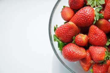 red strawberries in a glass bowl on the white background with a copy space