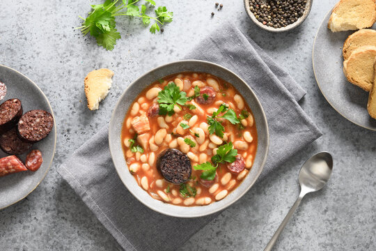 Traditional Spanish fabada served on gray stone background. Fabada makes of haricot, chorizo, morcillas or blood sausage, tomatoes. Top view. Asturiana popular cuisine.