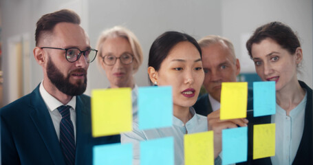 Young asian businesswoman explaining business strategy to staff in office reading notes on sticker