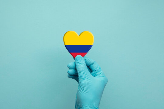 Hands wearing protective surgical gloves holding Colombia flag heart