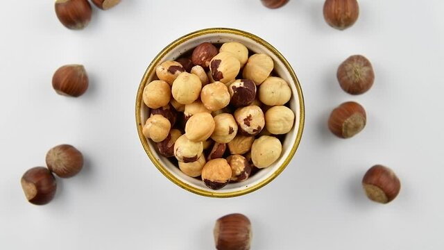 Peeled hazelnuts in a bowl and whole hazelnuts on a white wooden background, top view, zoom in