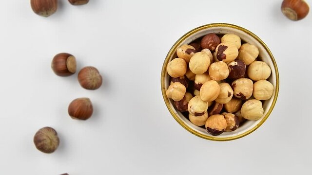 Peeled hazelnuts in a bowl and whole hazelnuts on a white wooden background, top view, zoom in