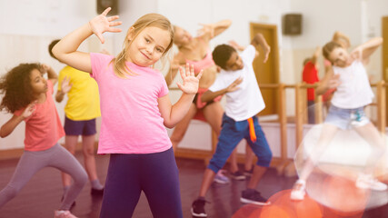 Smiling little girl training movements of vigorous dance with group of tweens in children dance...