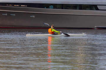 An unrecognizable young man is kayaking along the yacht