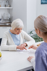 aged woman pointing with finger while playing jigsaw puzzle with social worker