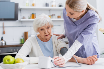 Obraz premium young nurse touching shoulder of senior woman while measuring her blood pressure