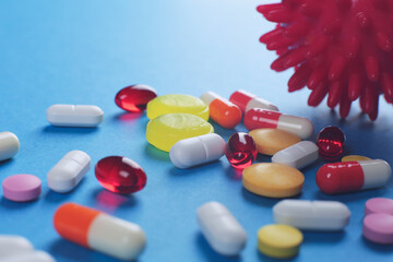 Multicolored medical pills of various shapes and imitation of a coronavirus cell on a blue background