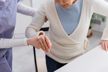 cropped view of social worker helping senior woman getting up