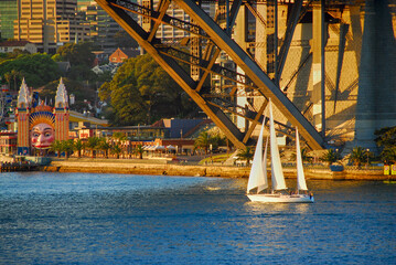 A sailboat sailing under the Harbour bridge on a early evening in Sydney's Darling Harbour in Australia.