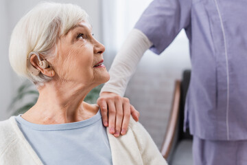 elderly woman with hearing aid looking at social worker touching her shoulder
