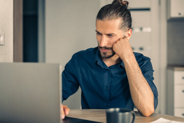 Concentrated frowning man working on laptop at home