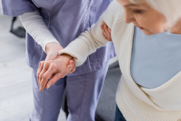 partial view of nurse supporting aged woman, blurred foreground