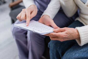 partial view of social worker pointing at calendar near aged woman sick on amnesia