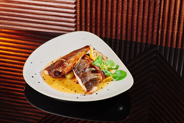White steak of grilled fish on pillow of vegetables and yellow sauce, with lemon slice and fresh...