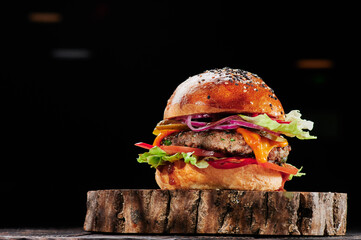 Beef burger with cheese, tomatoes, red onions, cucumber and lettuce on wooden cut on black background. Burger menu. Space for text. Unhealthy food. High quality photo - obrazy, fototapety, plakaty