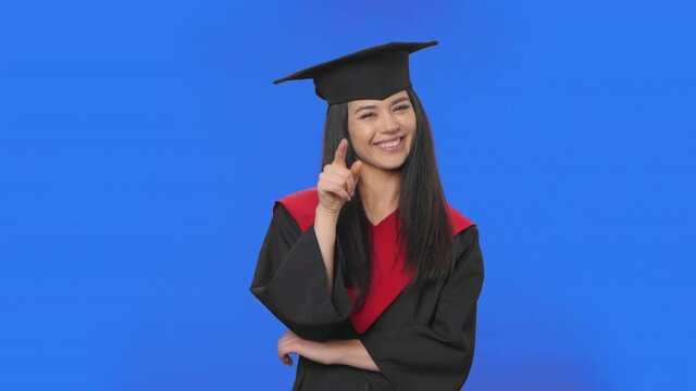 Portrait of female student in cap and gown graduation listening attentively, nodding, pointing finger at viewer. Brunette posing on blue screen background. Close up. Slow motion ready 59.94fps.
