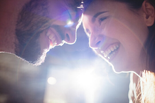Happy caucasian couple, touching heads together, laughing in a romantic moment, backlit by sunlight